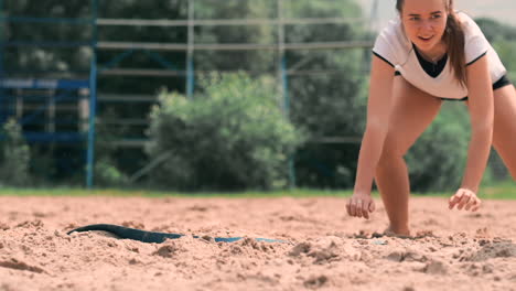 Young-female-athlete-dives-into-the-sand-and-saves-a-point-during-beach-volleyball-match.-Cheerful-Caucasian-girl-jumps-and-crashes-into-the-white-sand-during-a-beach-volley-tournament.